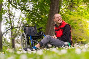 Young man sitting in front of wheelchair in park