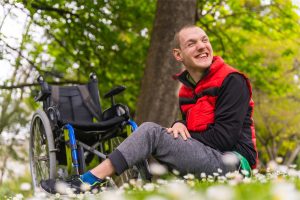 Young adult sitting in front of wheelchair in park