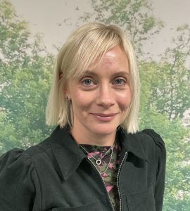 Emma against a greenery background, smiling at the camera