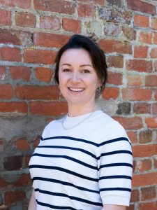 Kirsten against a brick wall, smiling at the camera